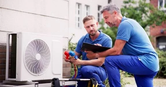 Two technicians assessing an outdoor air-conditioning system with a tablet and gauges